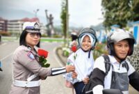 Anggota Satlantas Polres Tana Toraja yang memberikan bunga kepada salah satu anak sekolah, yang di bonceng, saat melintas di Plaza Kolam Makale, Tana Toraja, Rabu (23/07/25).
