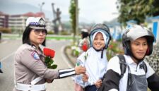 Anggota Satlantas Polres Tana Toraja yang memberikan bunga kepada salah satu anak sekolah, yang di bonceng, saat melintas di Plaza Kolam Makale, Tana Toraja, Rabu (23/07/25).