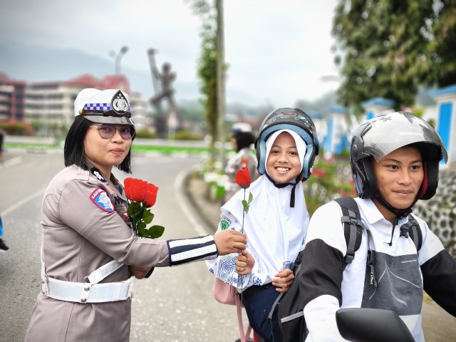 Anggota Satlantas Polres Tana Toraja yang memberikan bunga kepada salah satu anak sekolah, yang di bonceng, saat melintas di Plaza Kolam Makale, Tana Toraja, Rabu (23/07/25).